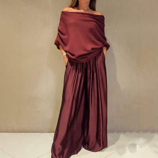 Şık, omuzları açıkta bırakan bir kazak ve saten bol paçalı pantolondan oluşan iki parçalı takım.